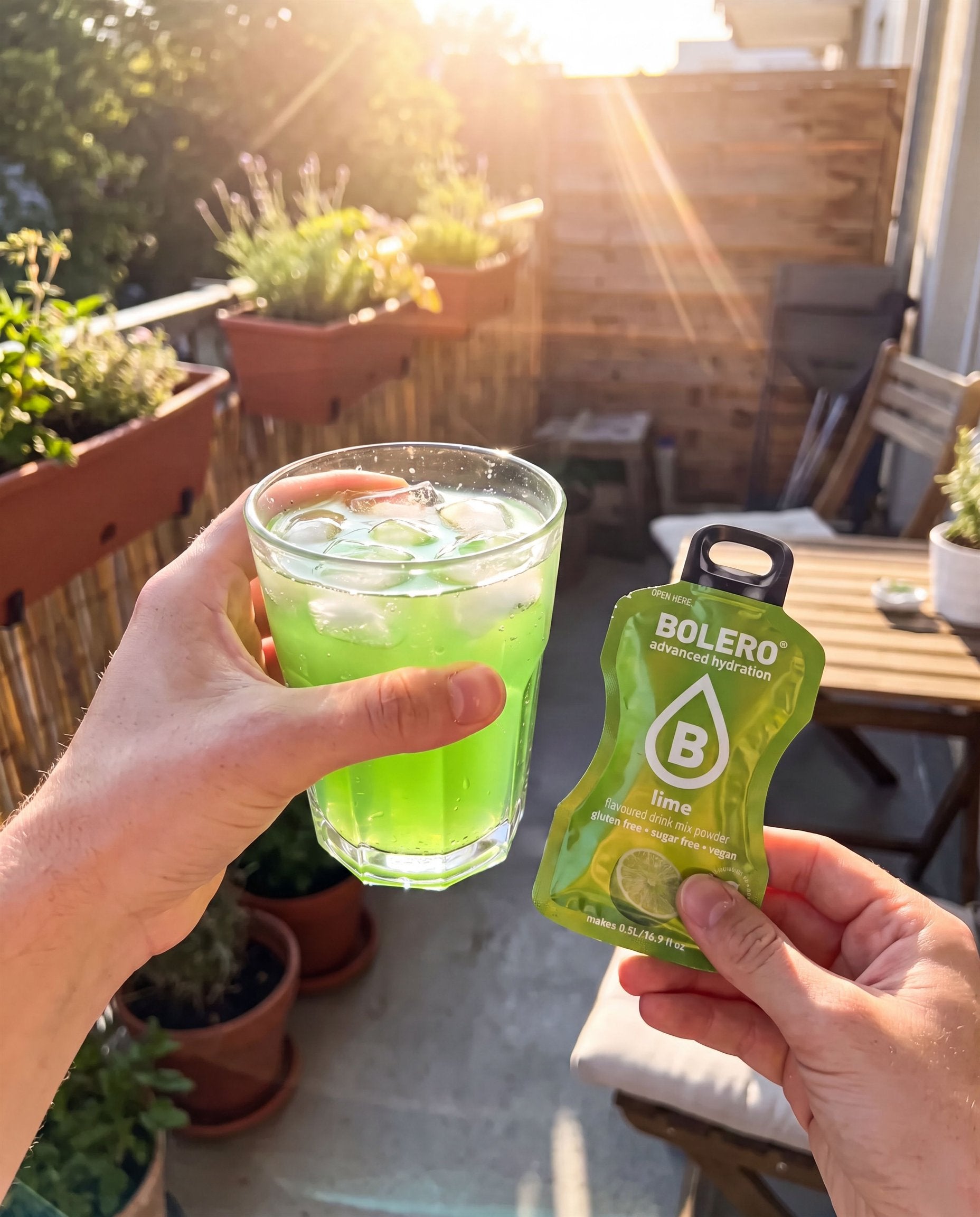 Glas mit grünem Limetten-Drink und ein Bolero-Päckchen auf einem sonnigen Balkontisch