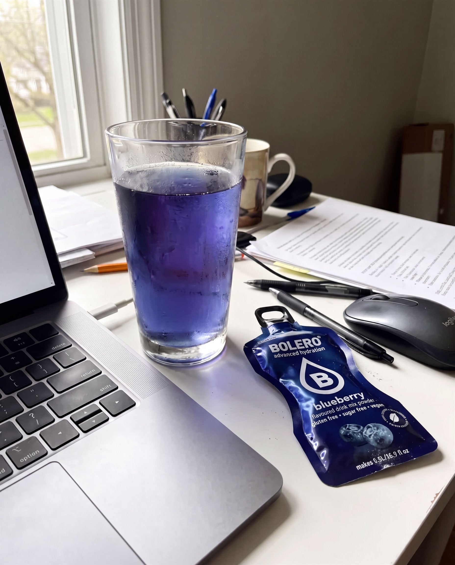 Glas mit blauem Heidelbeer-Drink neben einem Laptop, daneben ein Bolero-Päckchen
