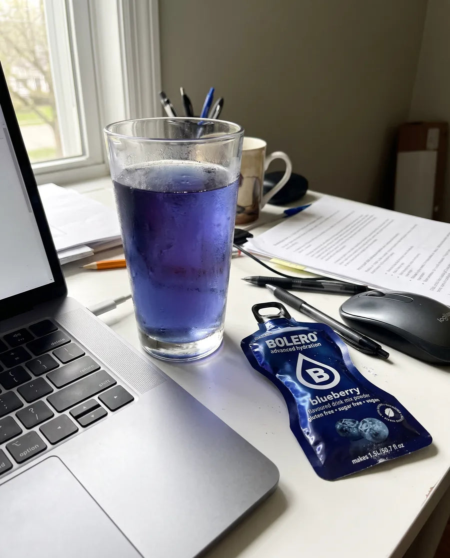 Glas mit blauem Heidelbeer-Drink neben Laptop im Homeoffice, daneben ein Bolero-Blueberry-Päckchen